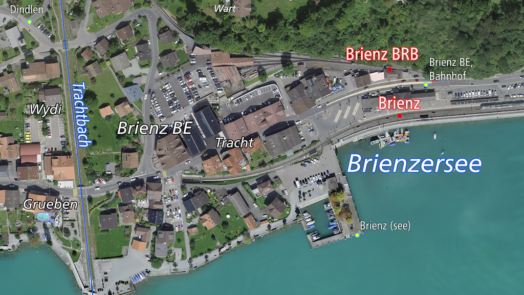 Das Bild zeigt eine Luftaufnahme von Brienz BE mit dem Dorf, dem Bahnhof und dem Brienzersee. 